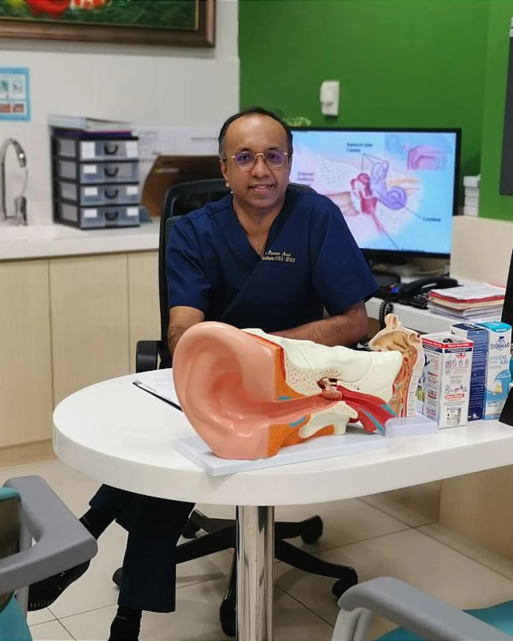 Dr Puvan at his desk with an ear model in the consultation room